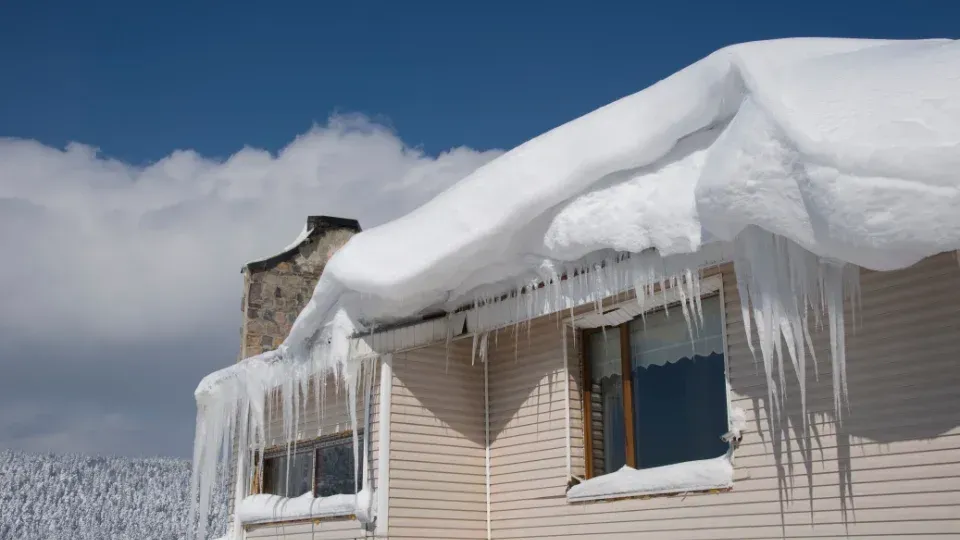 Snow-covered house roof with long icicles under a cloudy sky