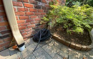 Coiled black cable beside a brick wall and downspout in a garden patio corner