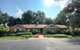 Single-story brick house with a landscaped front yard and driveway under a bright blue sky