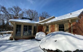 Snow-covered house with large drifts in a sunny winter yard