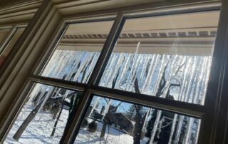 Snowy backyard viewed through a window with icicles hanging from the roof edge