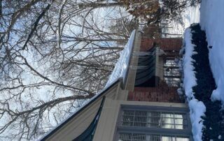 Snow-covered brick house with bare trees and a front porch in winter
