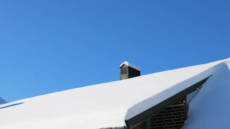 Snow-covered rooftop with a small chimney against a clear blue sky