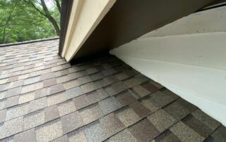 Roof shingles beside white siding under an eave, viewed from below.