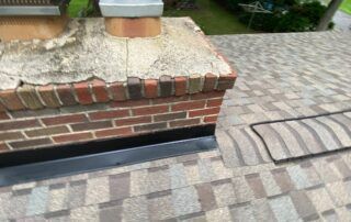 Brick chimney with damaged mortar and cracked concrete on a shingled roof