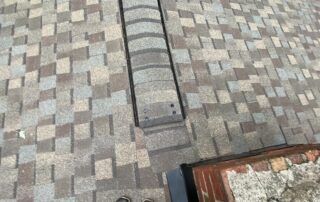 Close-up of a gray-brown shingled roof with a vertical vent pipe near the center.