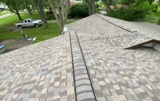 Roof with gray shingles and a central ridge, viewed from above with trees and a parked truck in the background