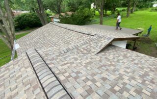 A sloped shingled roof in a green park, with two people walking nearby.
