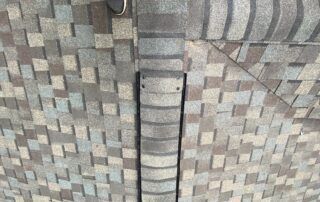 Close-up of a gray brick and shingle roof with a vertical vent pipe in the center