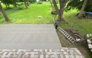 Backyard patio with gray pavers, lawn, trees, and a ladder beside a deck edge