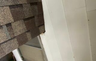 Close-up of roof shingles and a white exterior wall with a window edge.