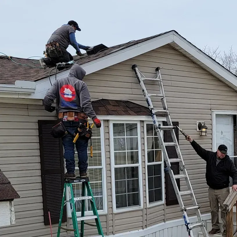 Workers repairing a house roof, with ladders and one person on the roof.