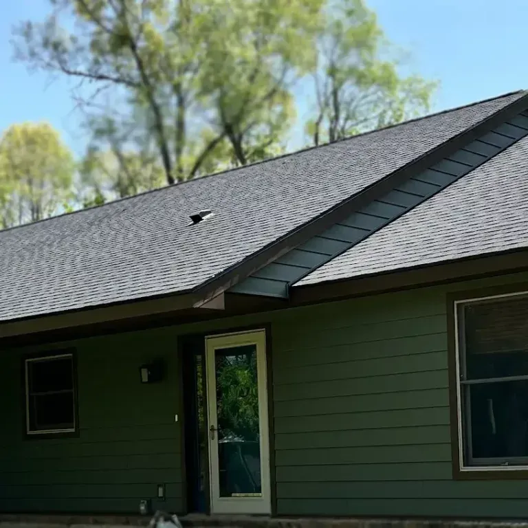 Green house exterior with dark roof, white-trimmed door, and windows under a blue sky