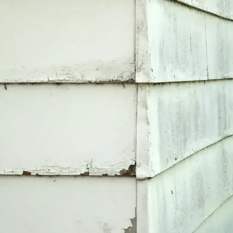 Peeling white paint and weathered siding at a building corner