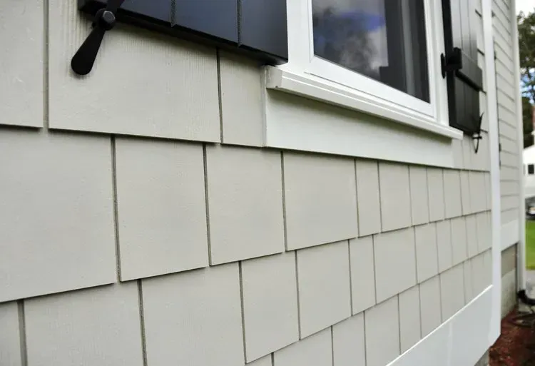 Close-up of gray siding on a house exterior with a white window and black shutter.