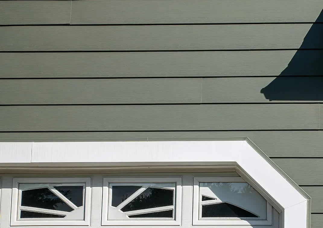 Green house siding with a white-trimmed bay window and triangular roof overhang