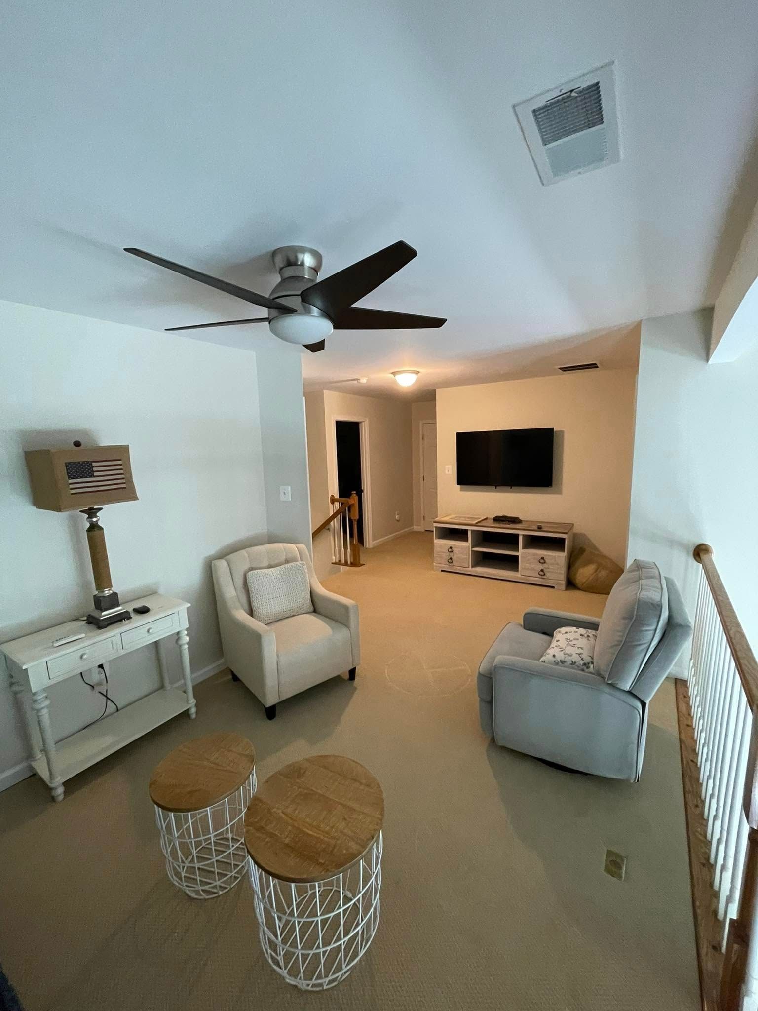 A living room with a ceiling fan , chairs , a couch and a television.