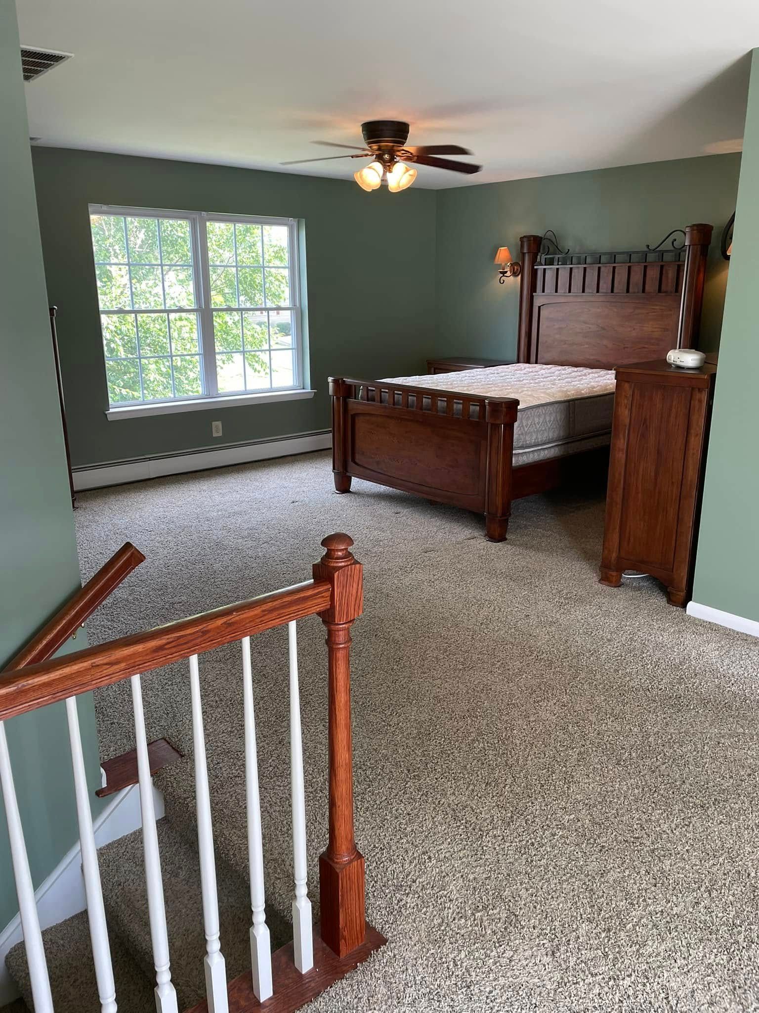 A bedroom with a bed , stairs and a ceiling fan.