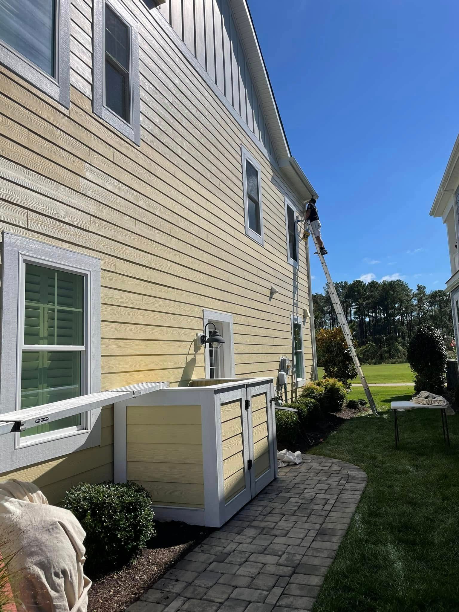 A man is painting the side of a house with a ladder.