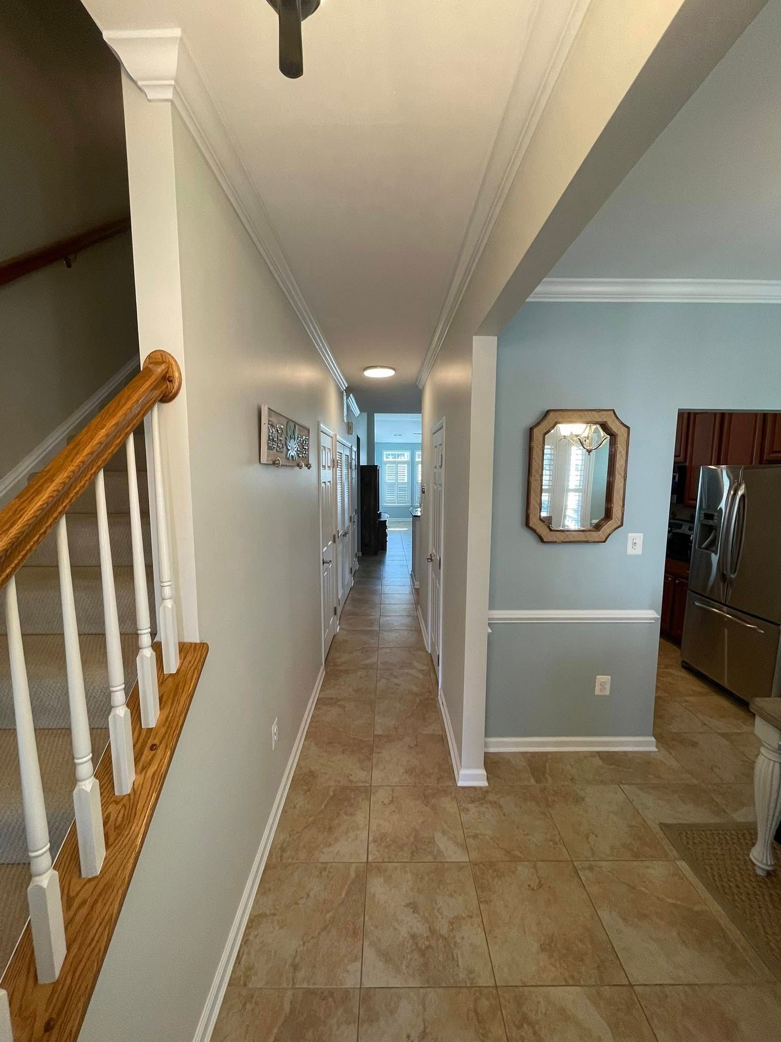 A long hallway in a house with stairs and a mirror on the wall.