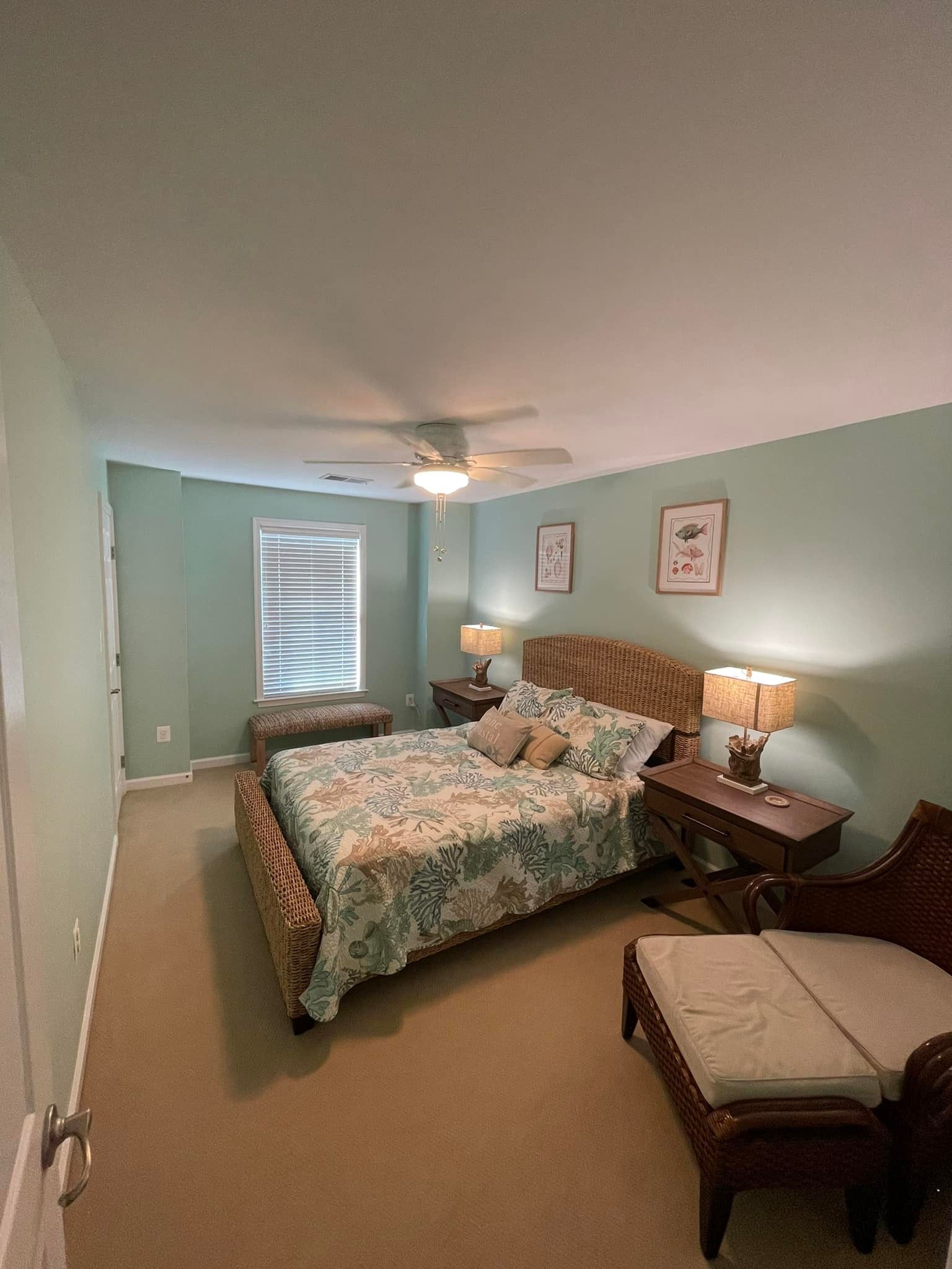A bedroom with a bed , chair , ottoman , lamps and a ceiling fan.