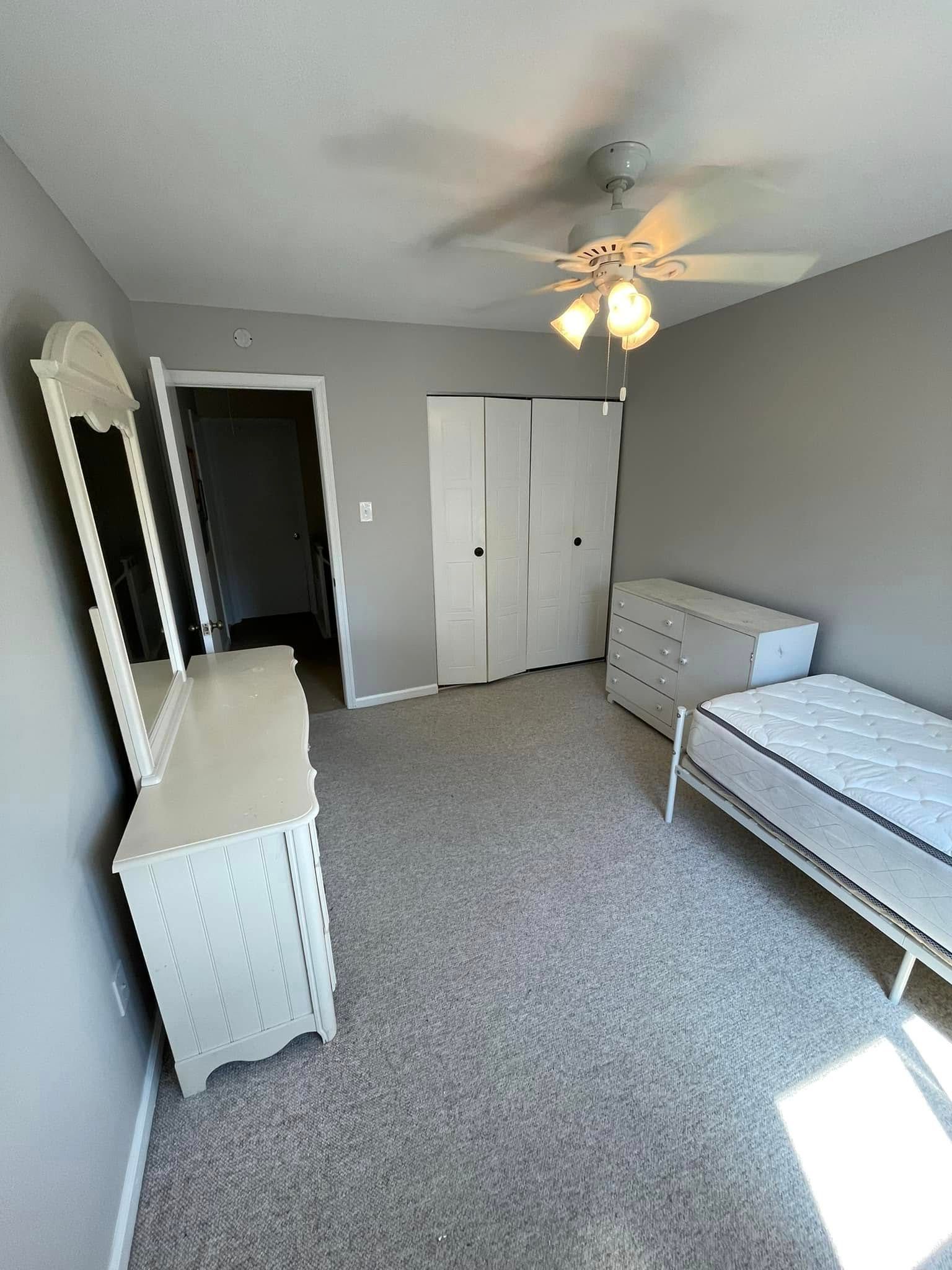 A bedroom with a bed , dresser , mirror and ceiling fan.