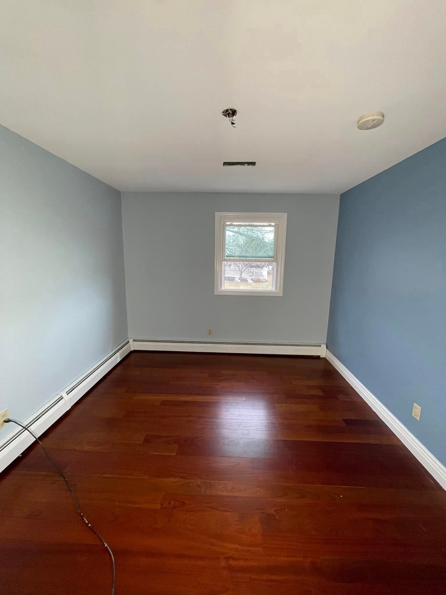 An empty room with hardwood floors , blue walls and a window.