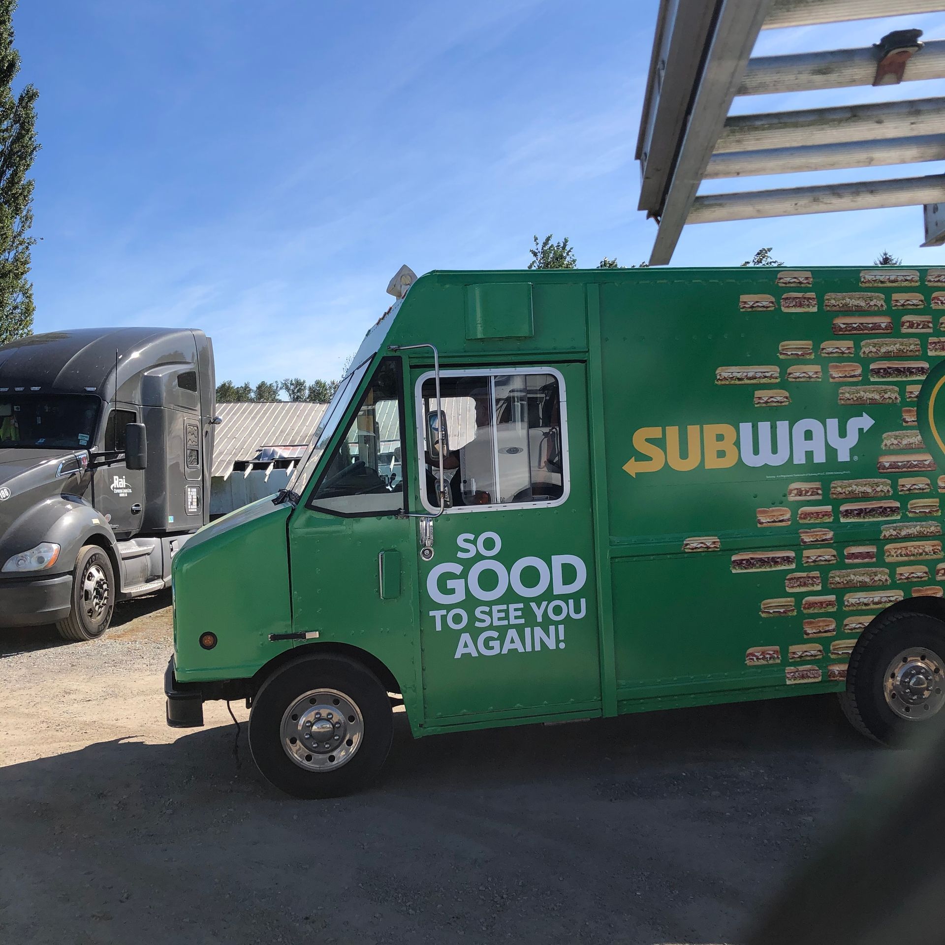A green subway truck is parked next to a truck