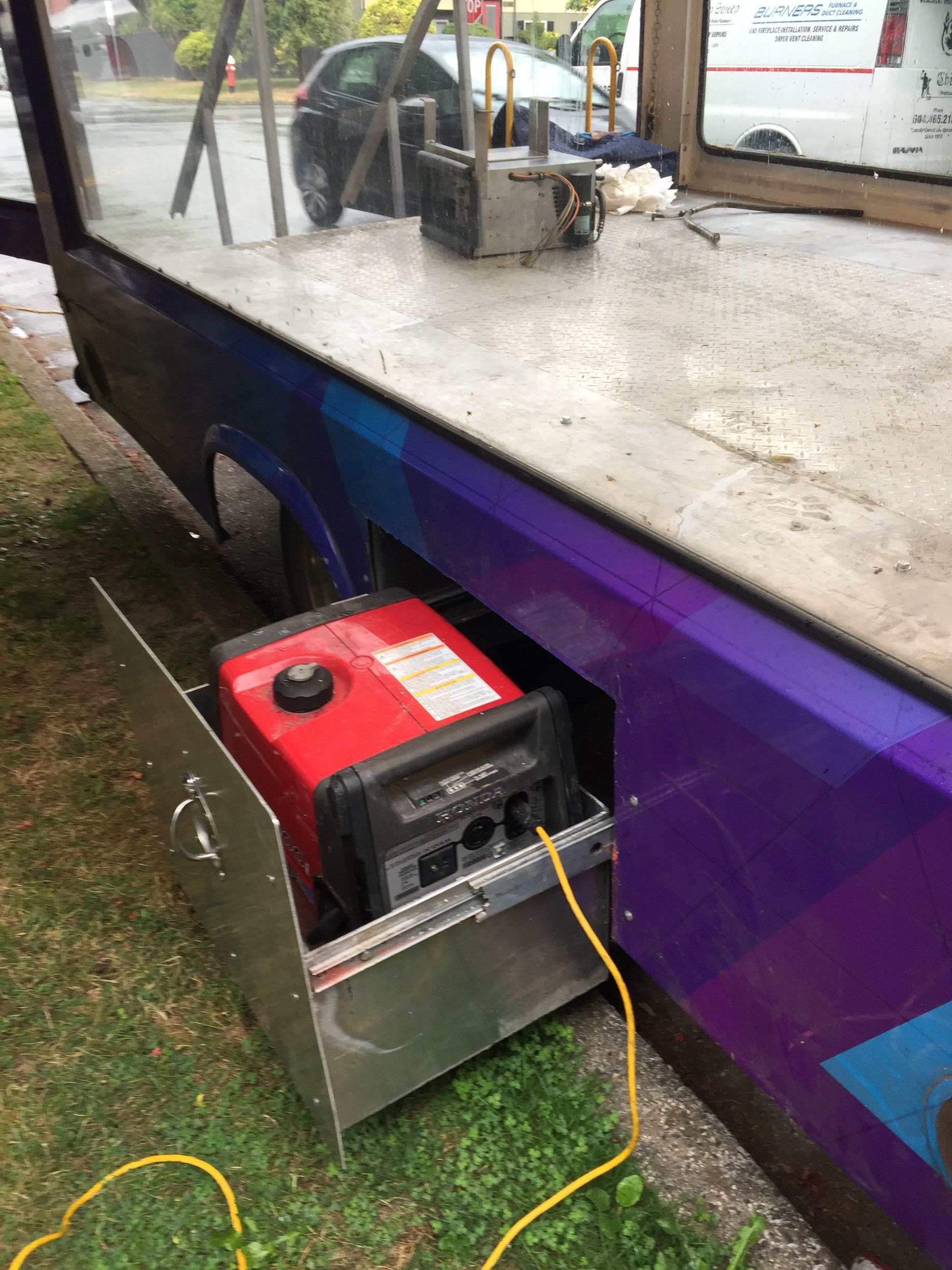 A red generator is plugged into the side of a truck.