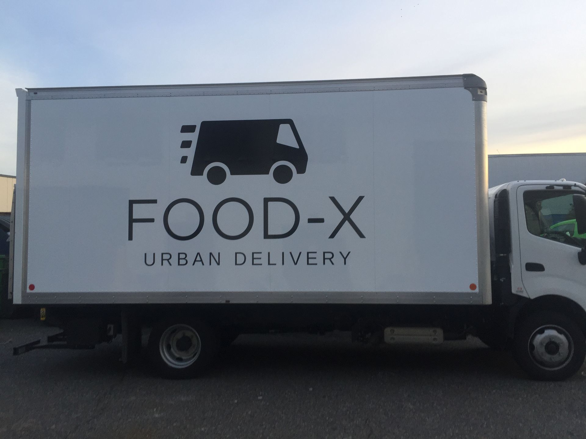 A food-x urban delivery truck is parked in a parking lot
