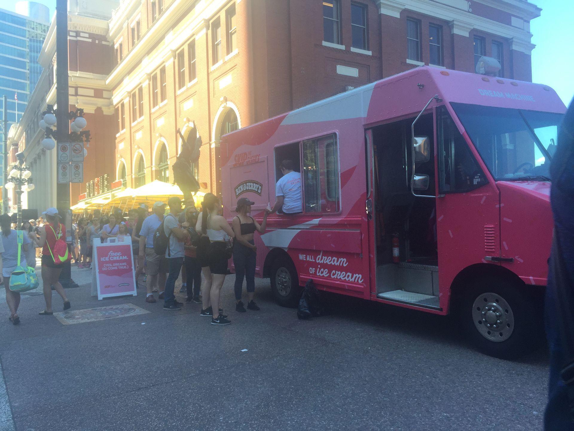 A pink food truck is parked in front of a brick building.