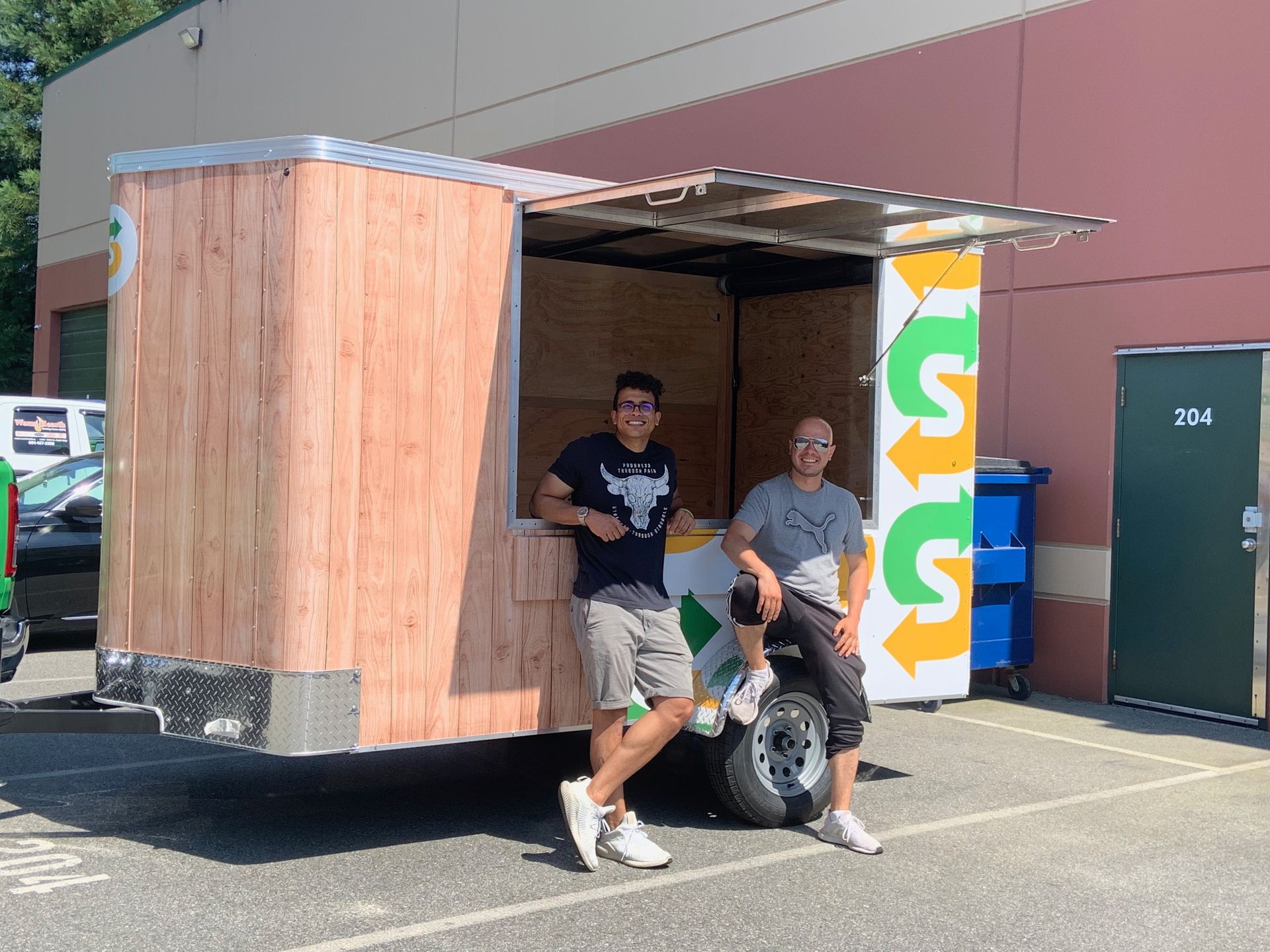 Two men are standing in front of a food truck in a parking lot.