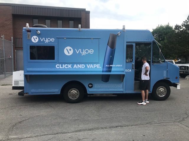 A man is standing next to a blue truck that says click and vape