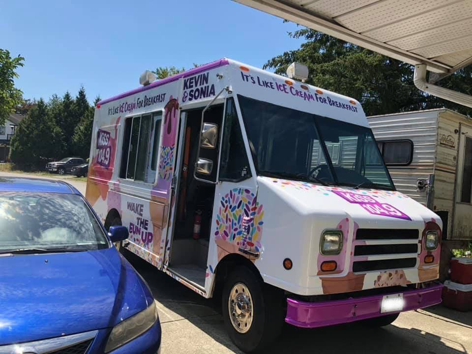 A purple and white ice cream truck is parked next to a blue car.