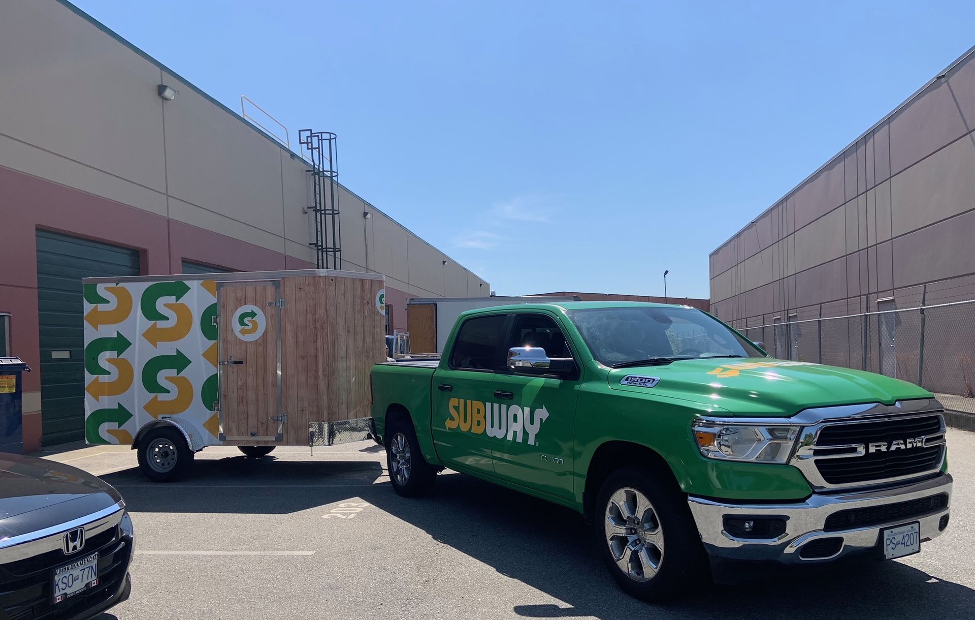 A green subway truck is parked in a parking lot next to a trailer.