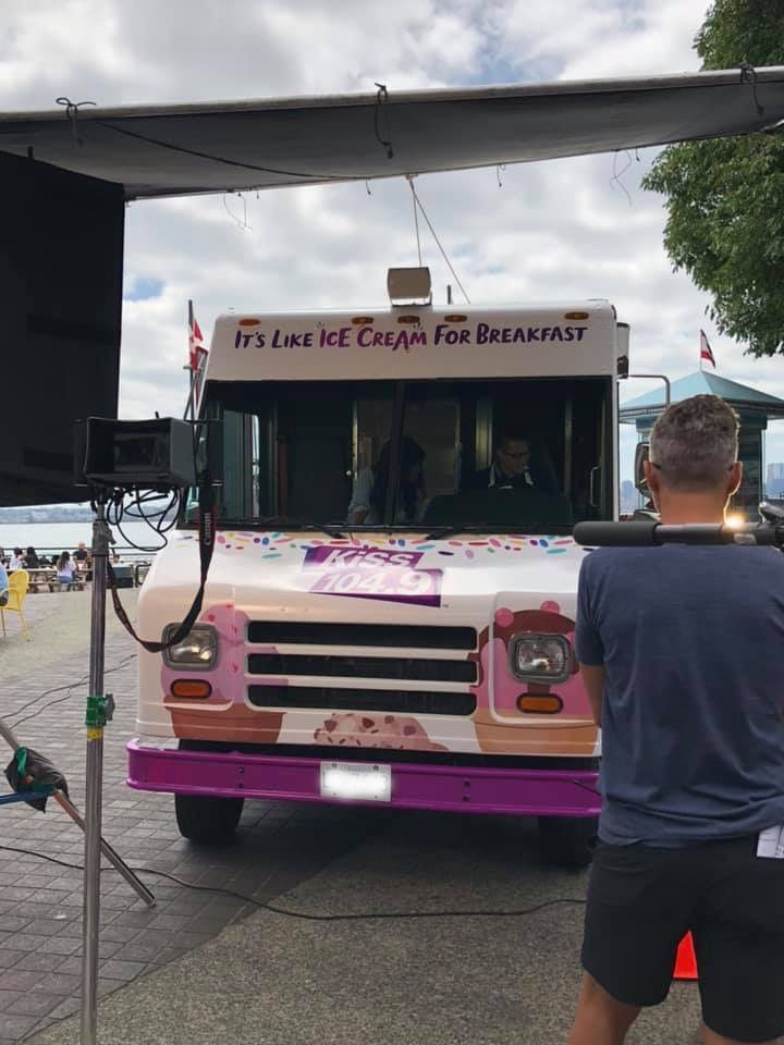 A man is standing in front of an ice cream truck that says it 's like ice cream for breakfast