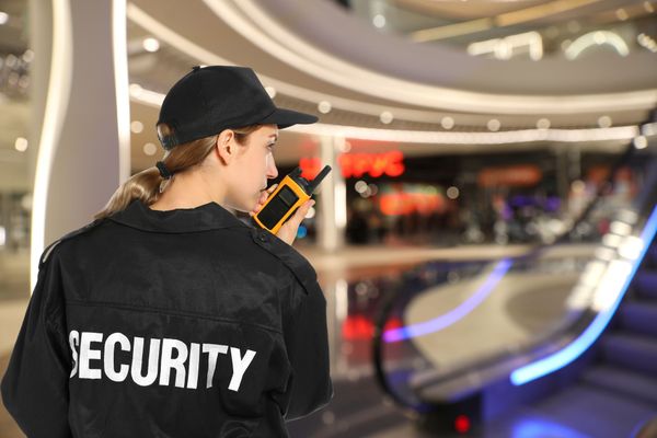 a woman in a security uniform is talking on a walkie talkie in a mall .
