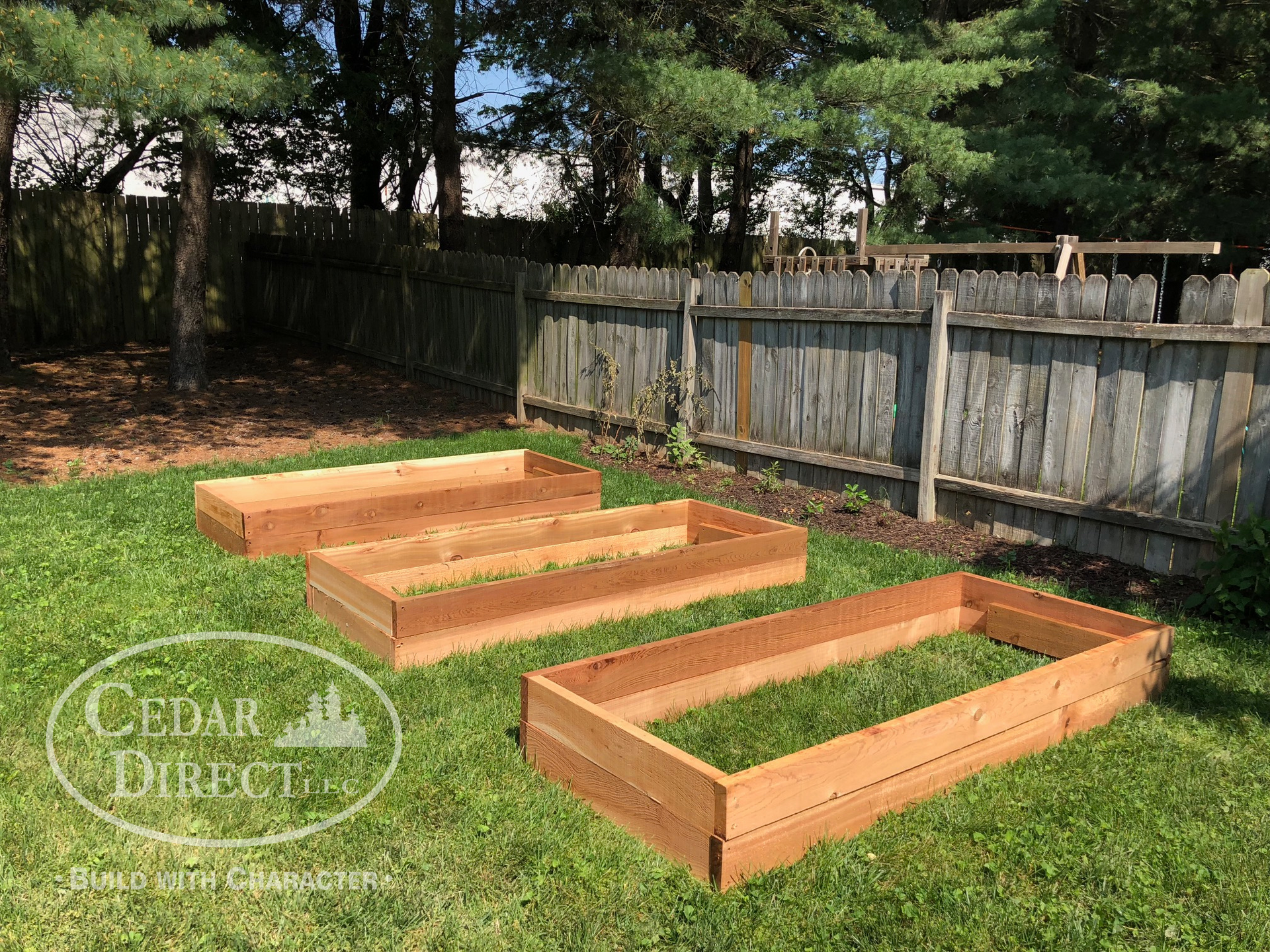 Three wooden raised garden beds are sitting in the grass next to a fence.