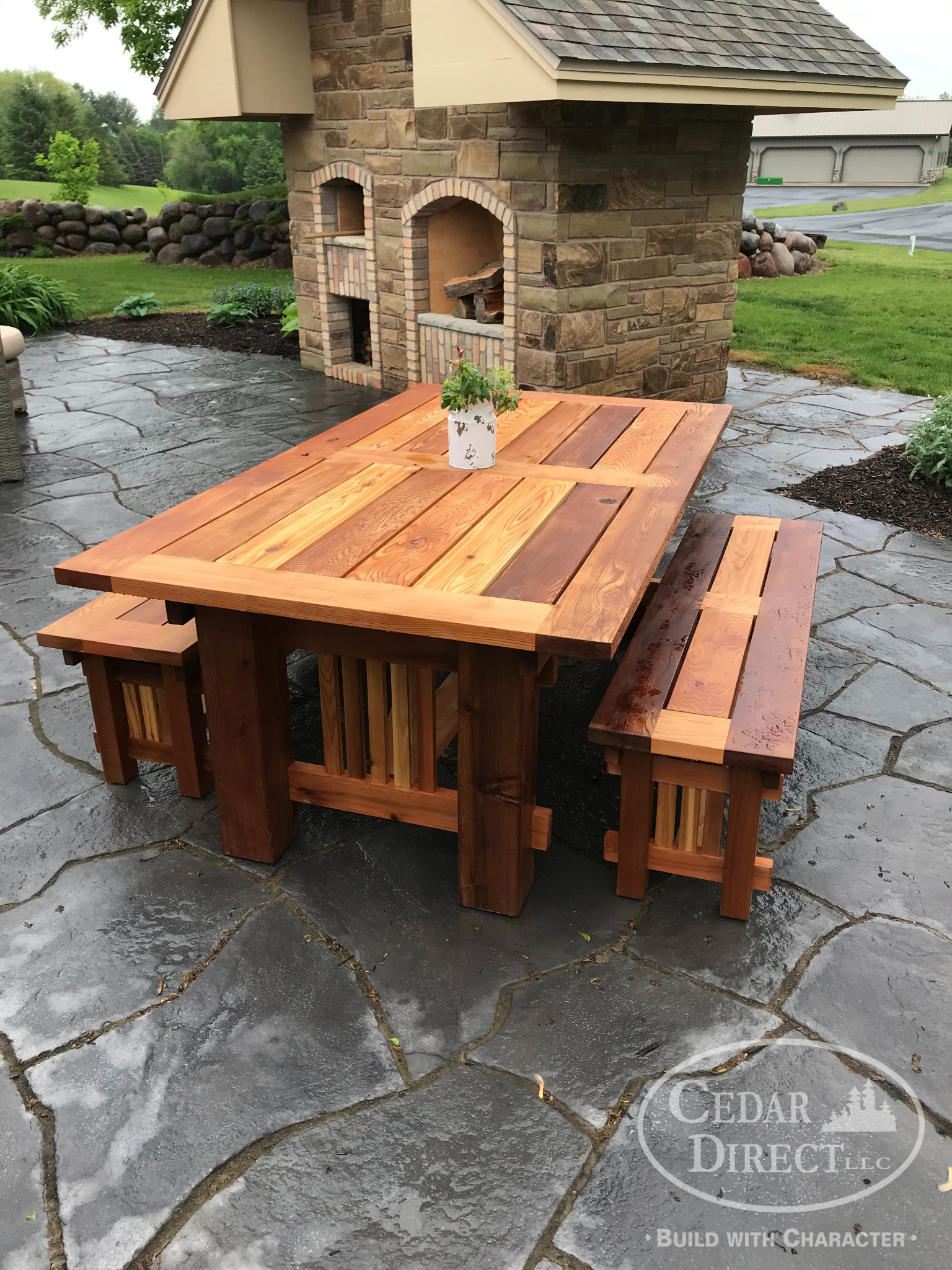 A wooden table and benches on a patio in front of a stone building.