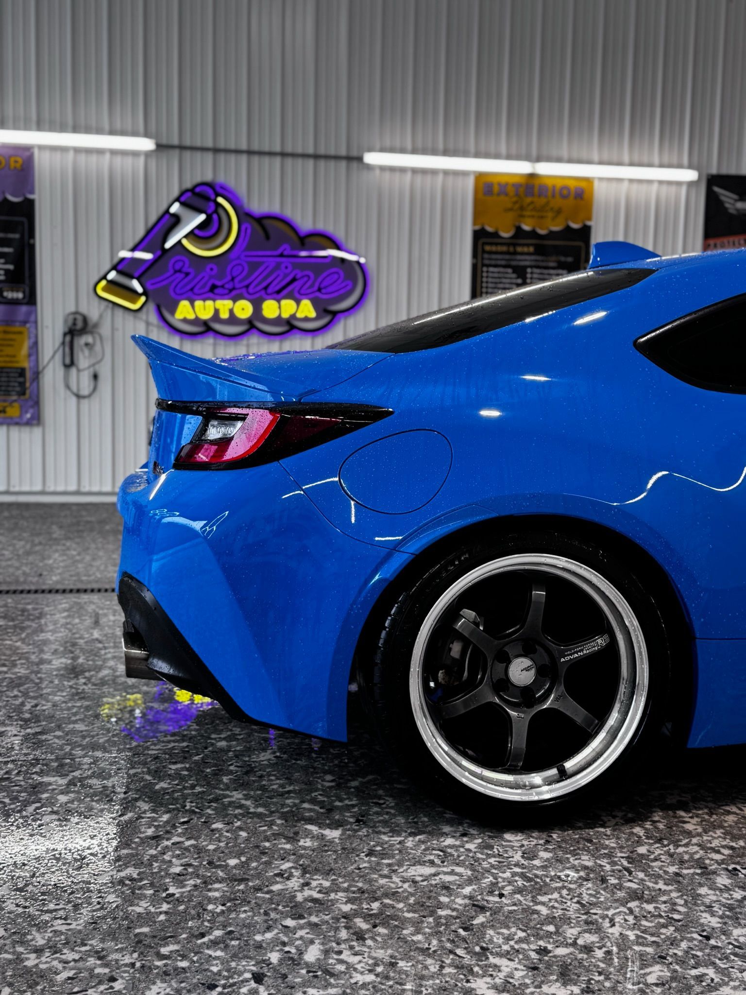 Hand with black glove wiping blue car surface with white cloth.