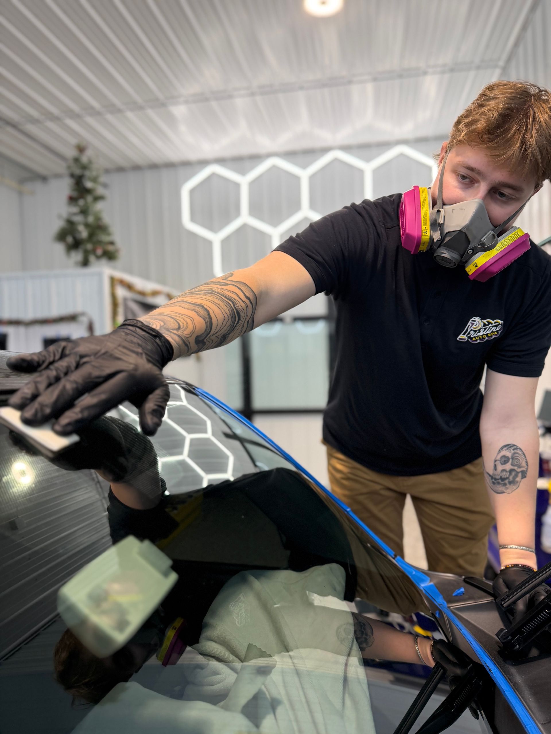 Person wearing black gloves cleaning a shiny black car with a blue sponge.