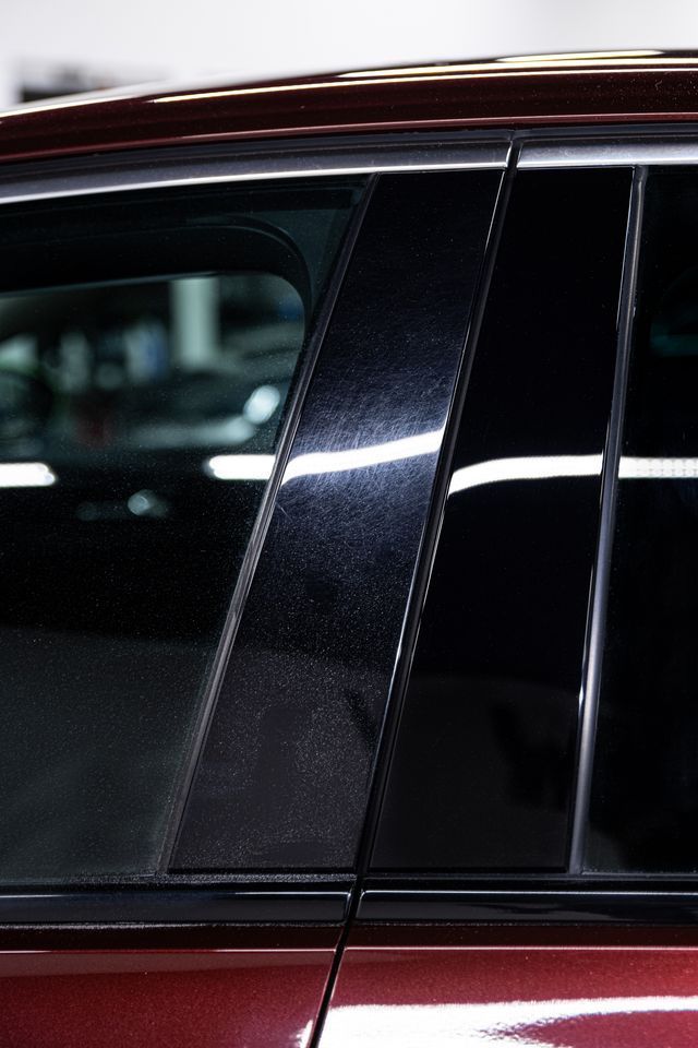 Person using a rotary polisher on a car's red taillight. Black gloves, white car, close up.