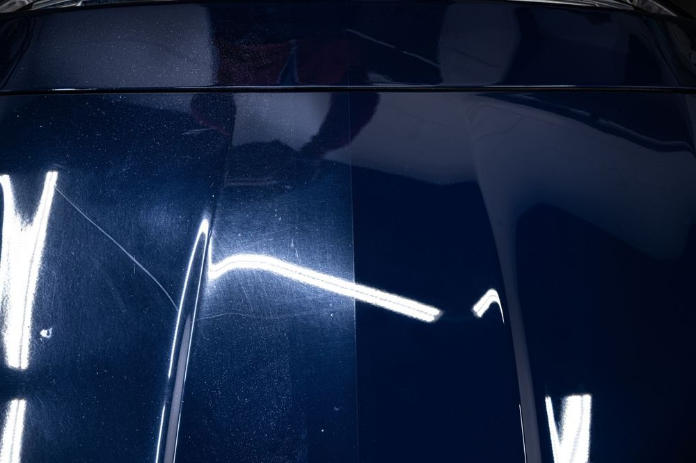 A person uses a red and black power buffer to polish a black car tail light.