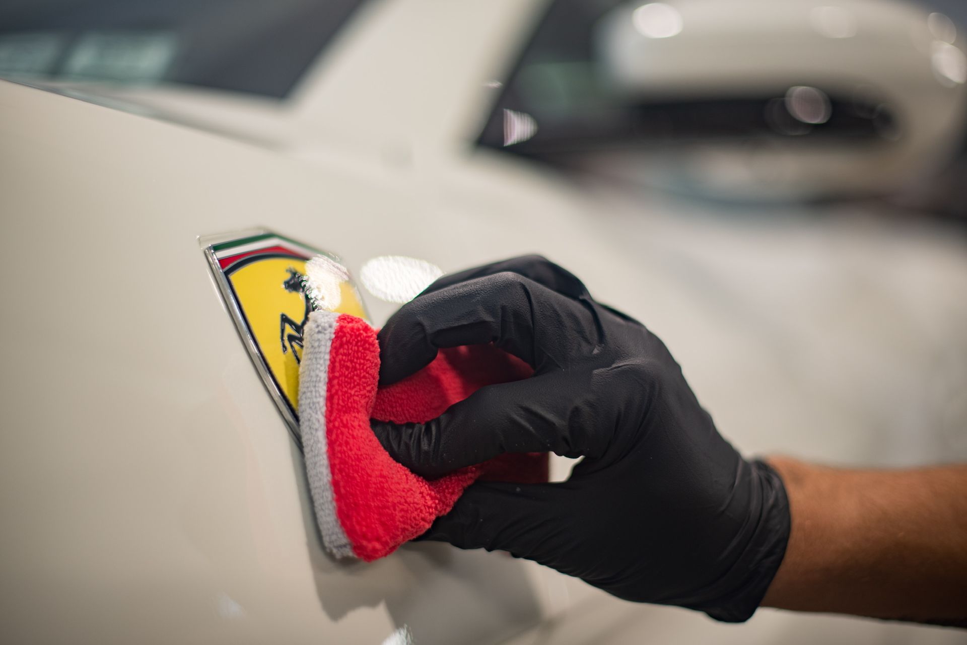 Person wearing black gloves applying product to blue car with a red applicator.
