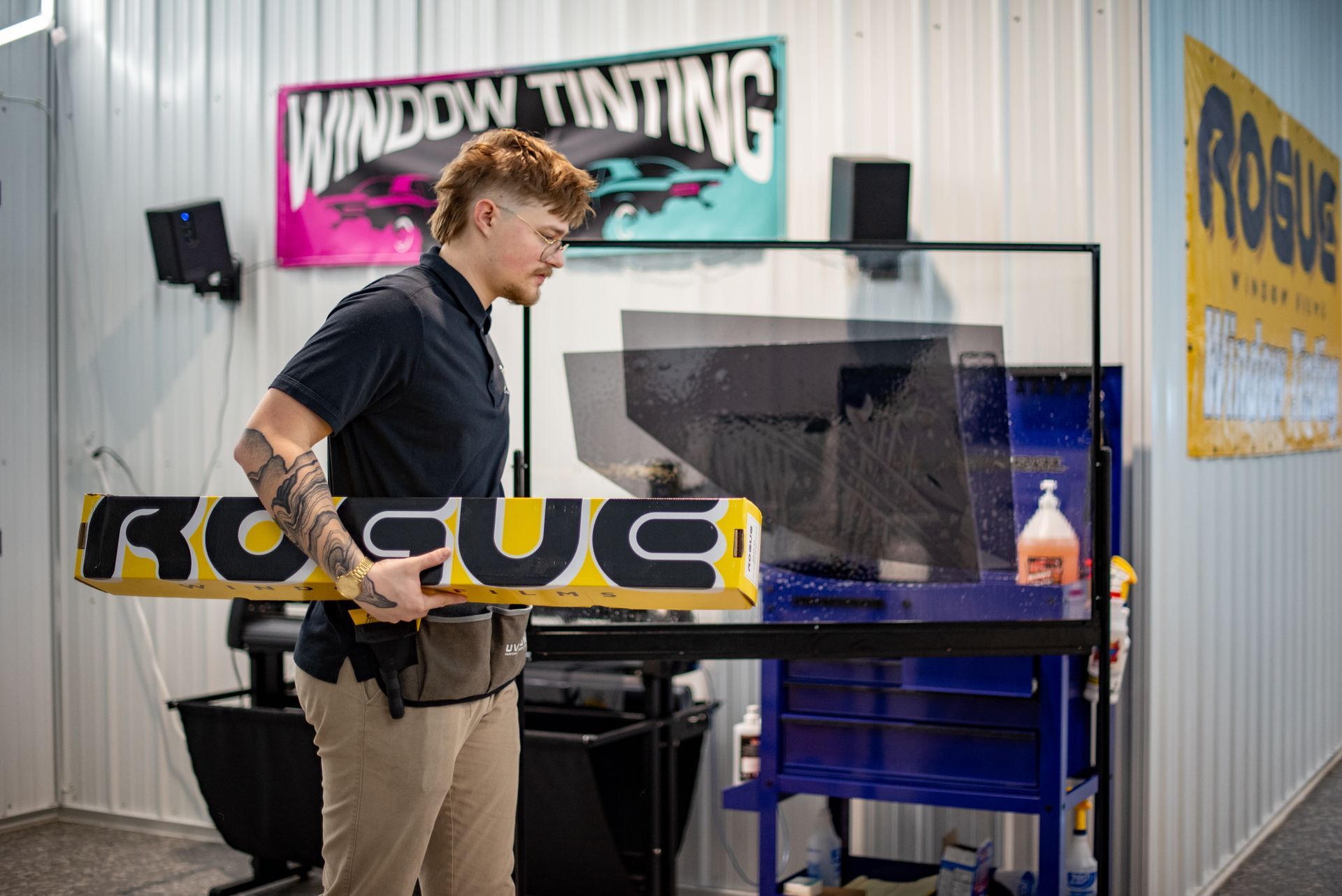 Man holding a Rogue-branded yellow and black tool, preparing to tint a car window in a shop.