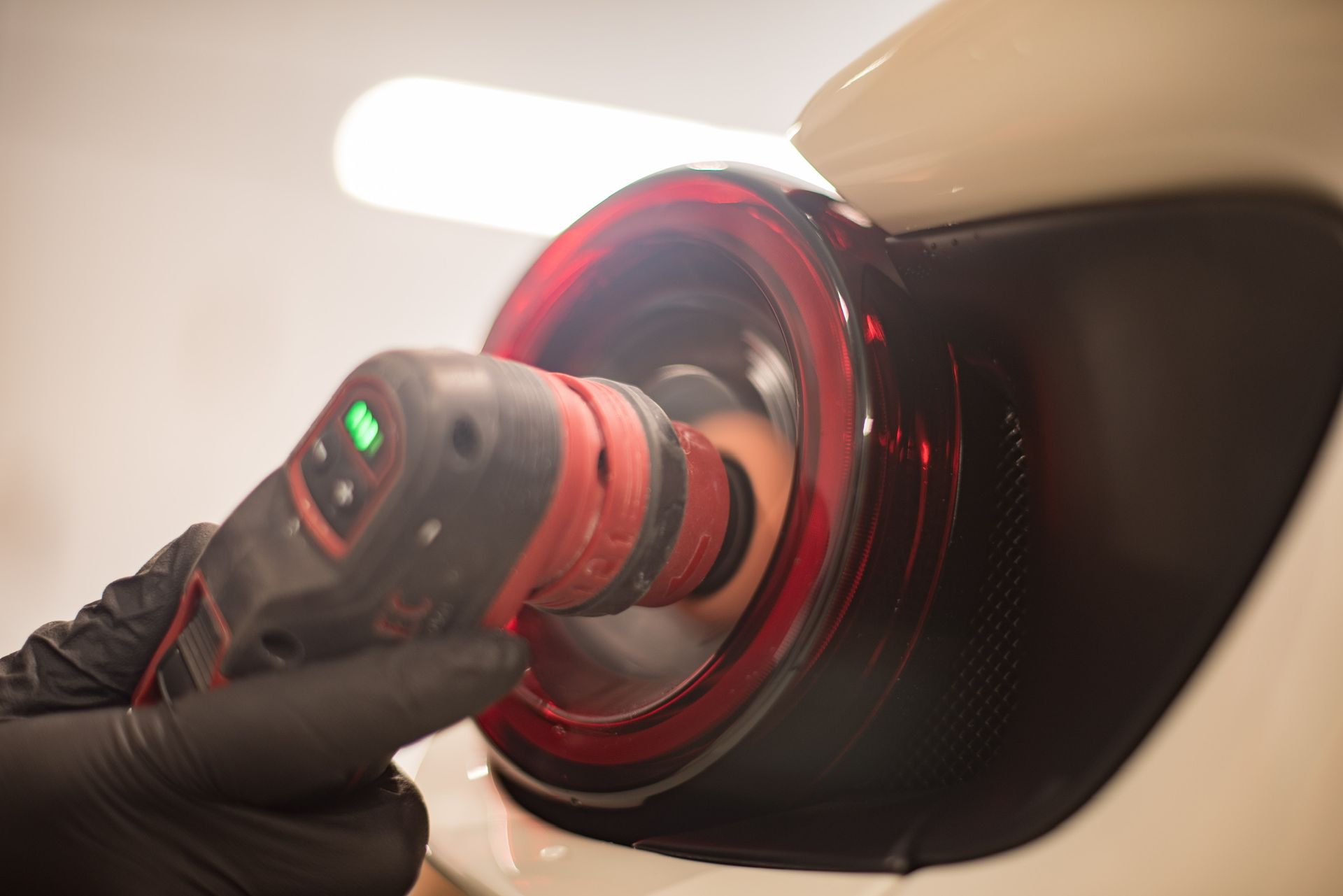 A person uses a red and black power buffer to polish a black car tail light.