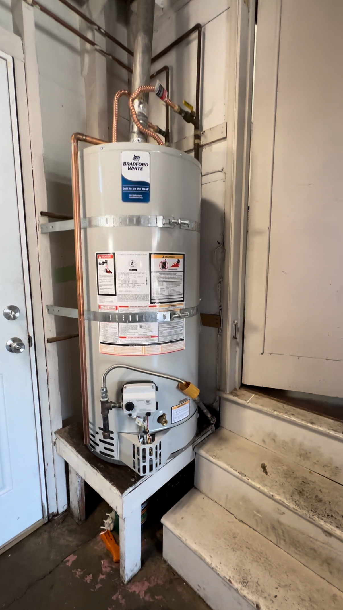 A water heater is sitting on a stand in a room next to stairs.