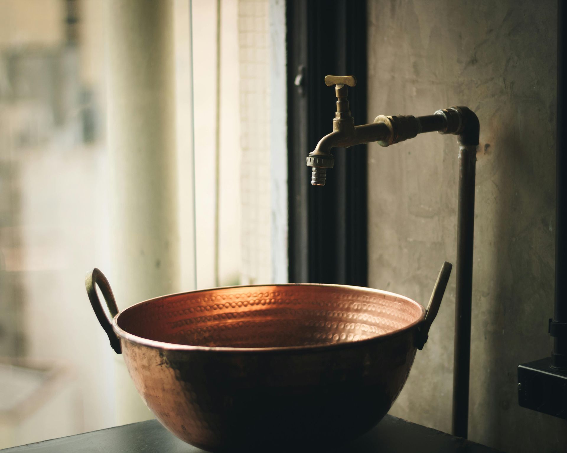 A copper bowl sits on a table next to a faucet