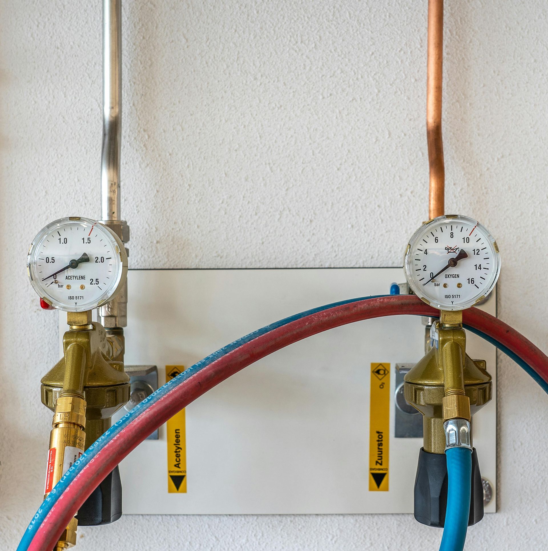 Two pressure gauges are mounted to a wall next to two hoses