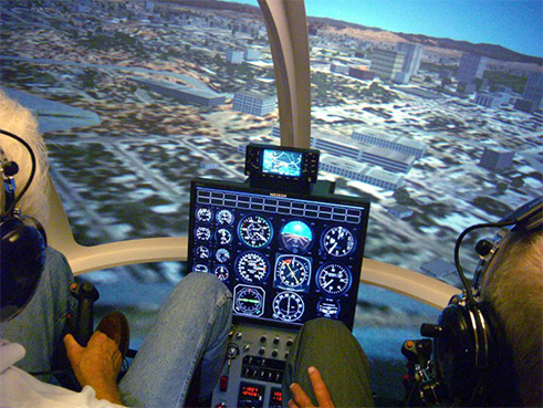 Inside a helicopter simulator cockpit, displaying instrument panel and projected cityscape.